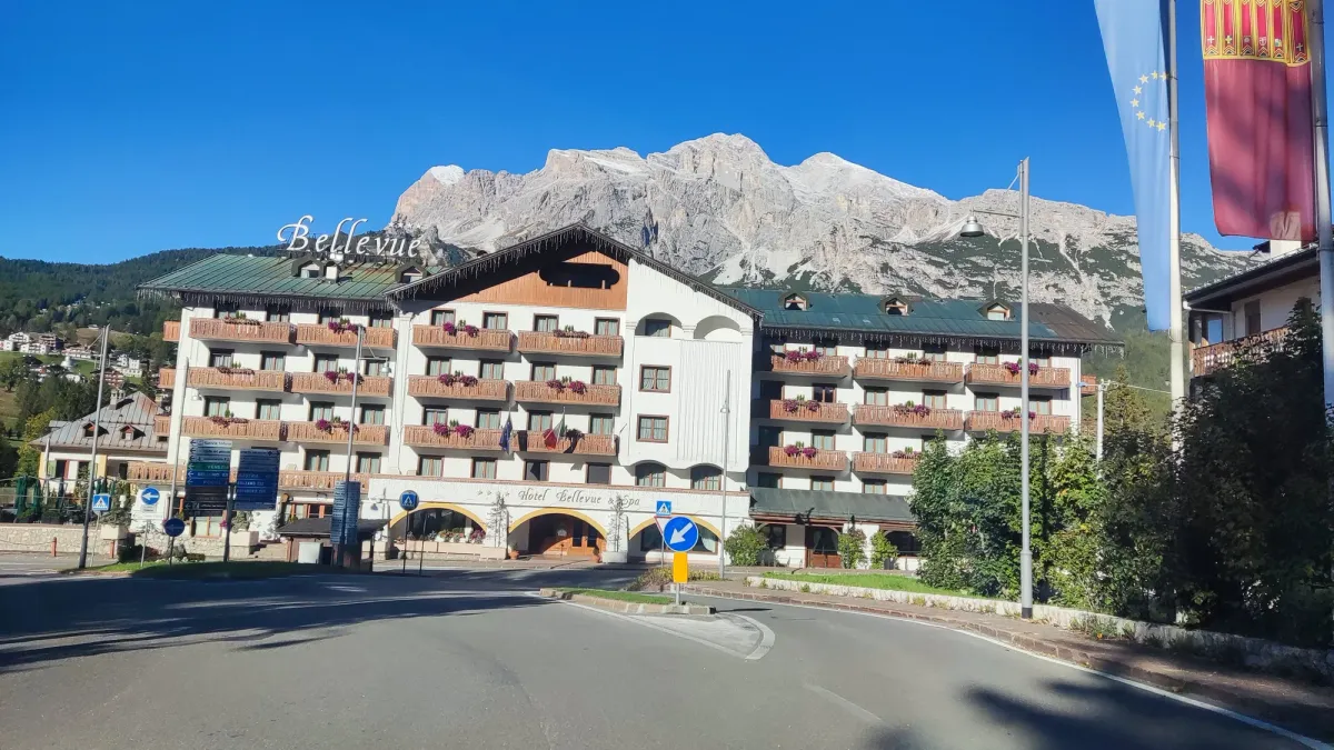 Vista externa do Hotel Bellevue & Spa em Cortina d'Ampezzo com a imponente montanha rochosa ao fundo sob um céu azul profundo