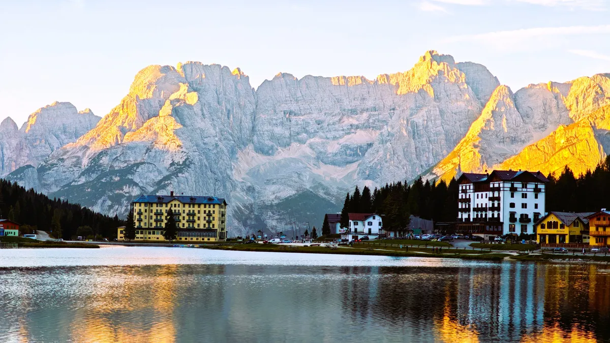 Lago di Misurina ao pôr do sol com os picos das Dolomitas coloridos pela Enrosadira, refletidos na água calma do lago.
